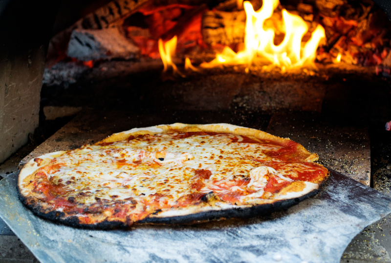 Image is of a pizza pie in the opening of a wood fired brick oven, concept of best pizza near Music Row in Nashville