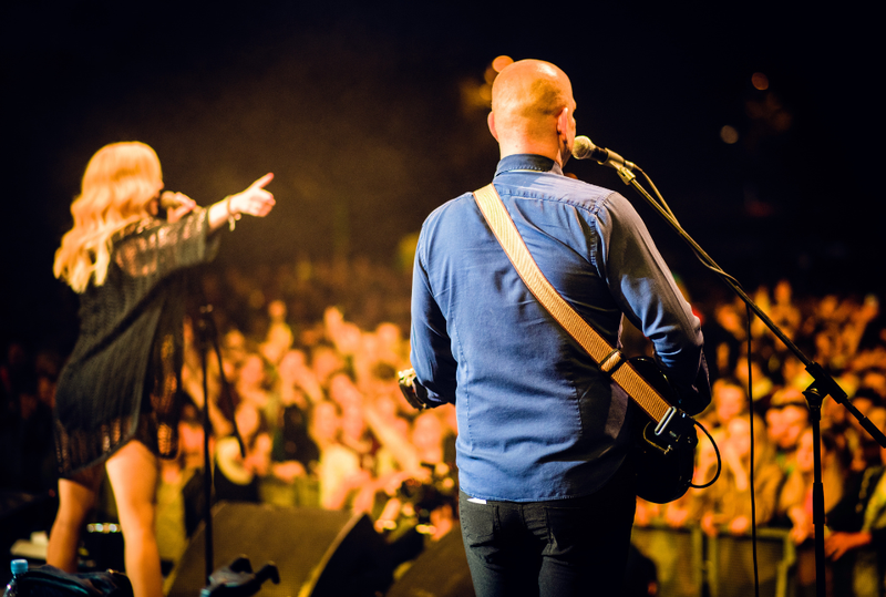 Image is of a man and woman on a stage singing to a large crowd of people, concept of guide to Country Music Awards