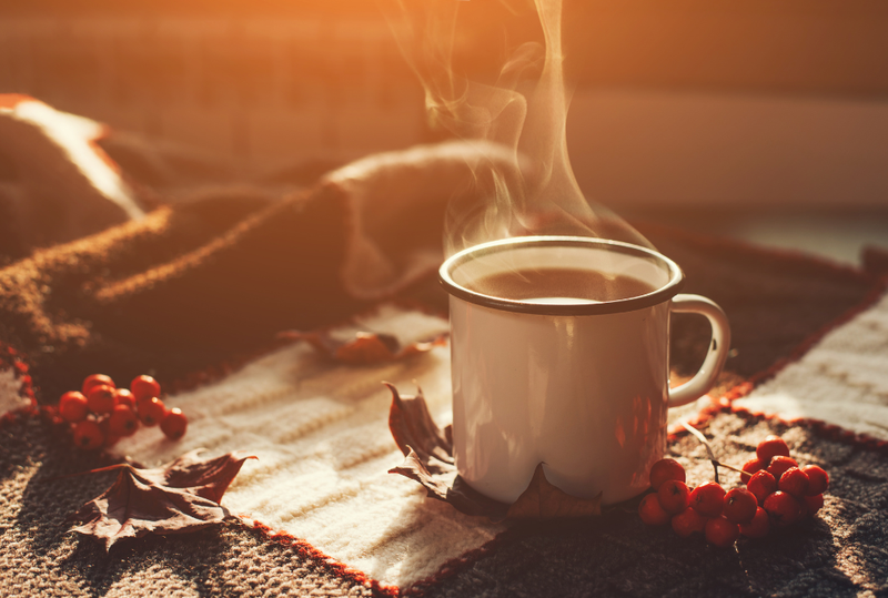 Image is of warm beverage in a mug sitting on a table with autumn leaves, concept of the Best Nashville cafes for fall treats