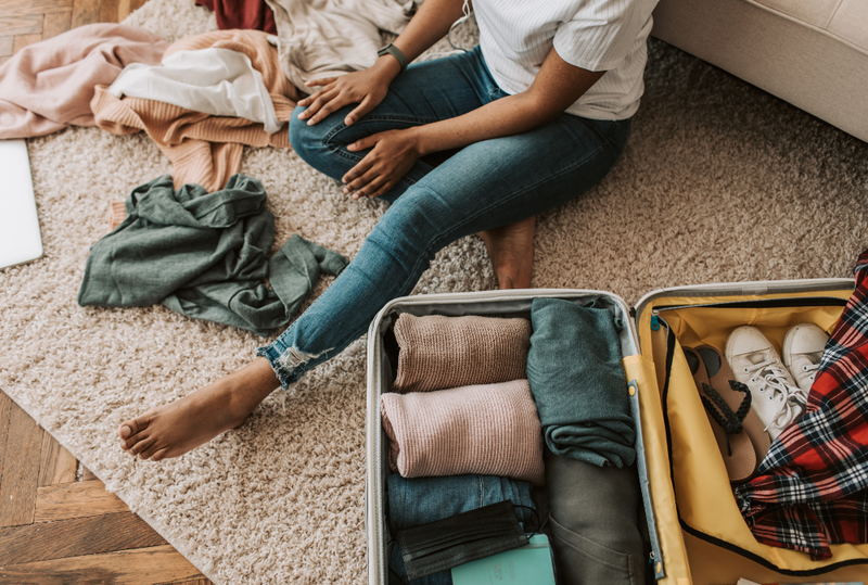 Image is of a woman sitting on her bedroom floor packing clothes in a suitcase, concept of packing for a winter visit in Nashville