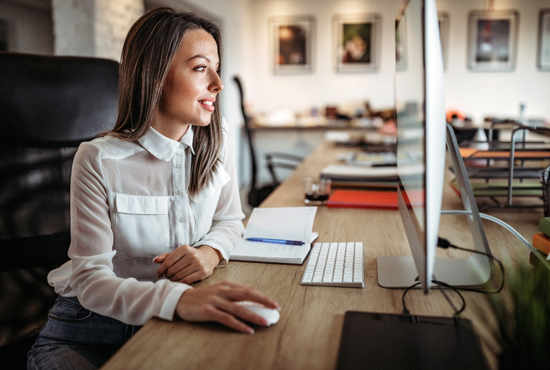 Image is of a woman sitting at a desk and on her computer searching for places to stay in a business trip, concept of corporate housing vs Airbnb for business travel
