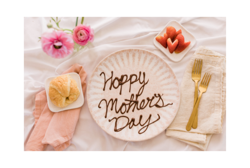 Breakfast in bed setup with a plate that has Happy Mother's Day written in chocolate syrup with pink flowers around it, concept of ways to celebrate Mother's Day in Nashville