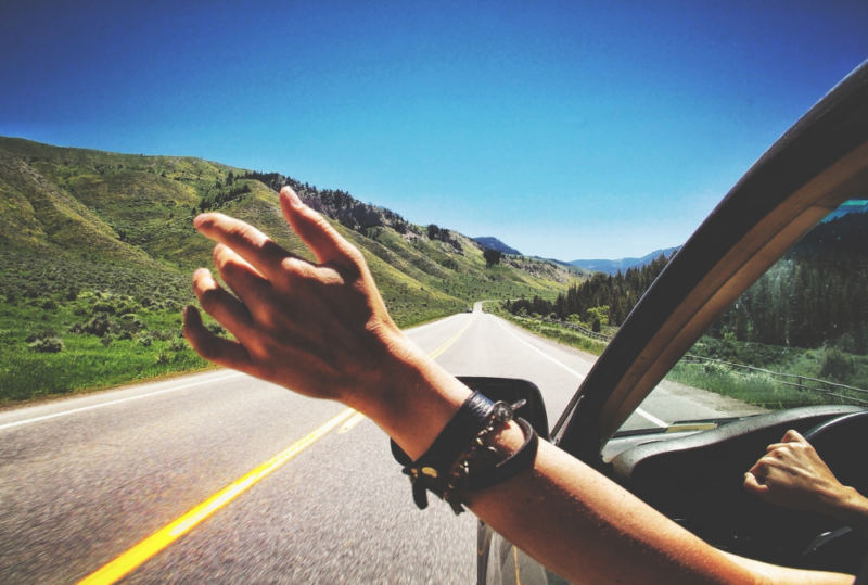 Image is of a person's hand outside of the car window feeling the wind as they are driving down the road, concept of easy day trips from Nashville