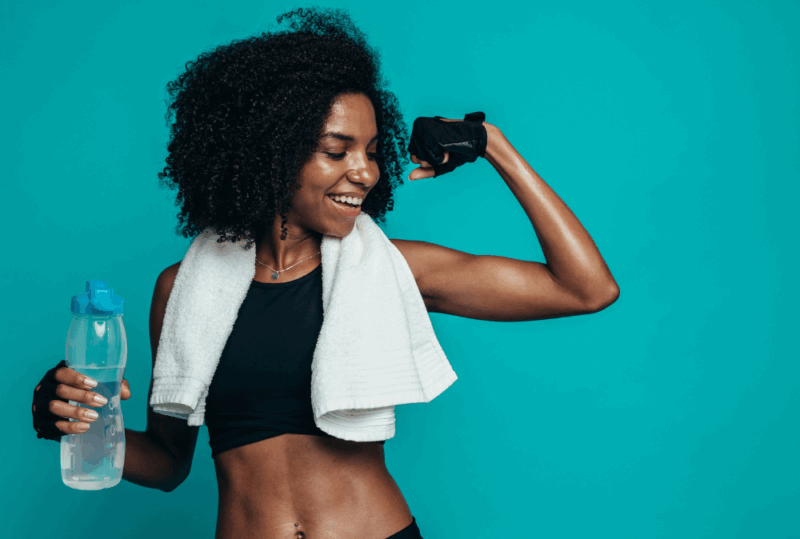 Image is of a young woman in workout gear, flexing her arm muscle following a workout, concept of staying fit during extended travel